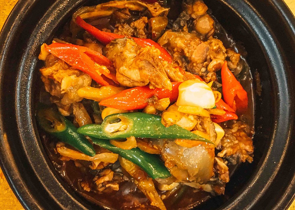 A black plate is filled with a Cambodian dish filled with chicken and green and red bell peppers.