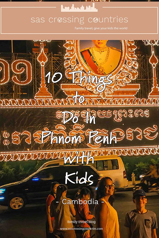 Cover image for a family travel blog post titled "10 things to do in Phnom Penh with kids" showcasing a mother and son at night in front of a lit up shrine for and photo of the king of Cambodia in Phnom Penh. The blog URL "www.sascrossingcountries.com" is visible at the bottom.