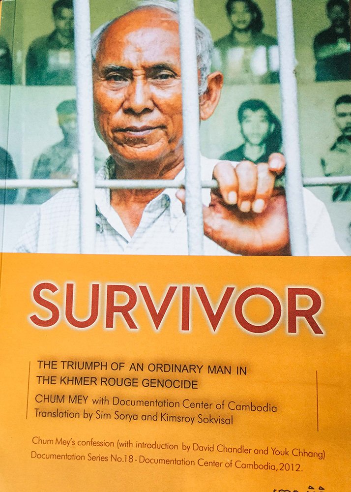 Book cover titled Survivor by Chum Mey. Chum survived years in Tuol Sleng. On the cover he poses in a white shirt in front of the white prison bars in what is now the genocide center.
