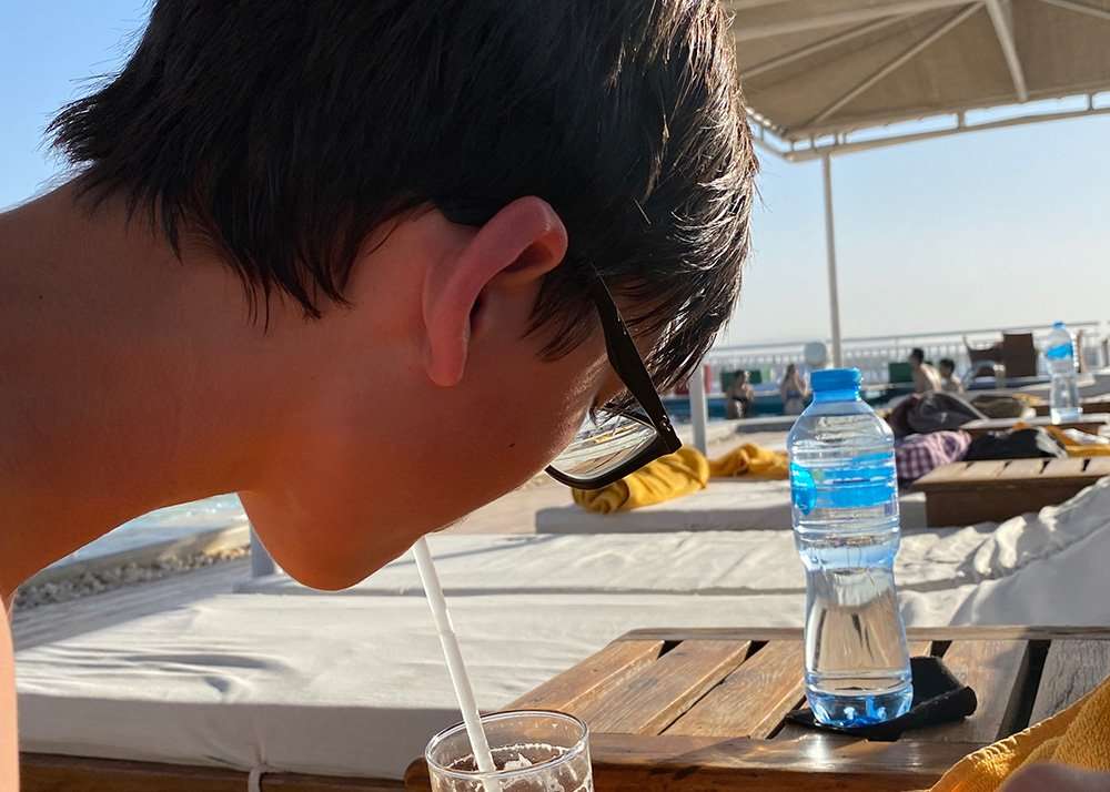A teen lying on a sun bed sipping from a lemon juice in a cocktail glass enjoying the view of the Nile river.