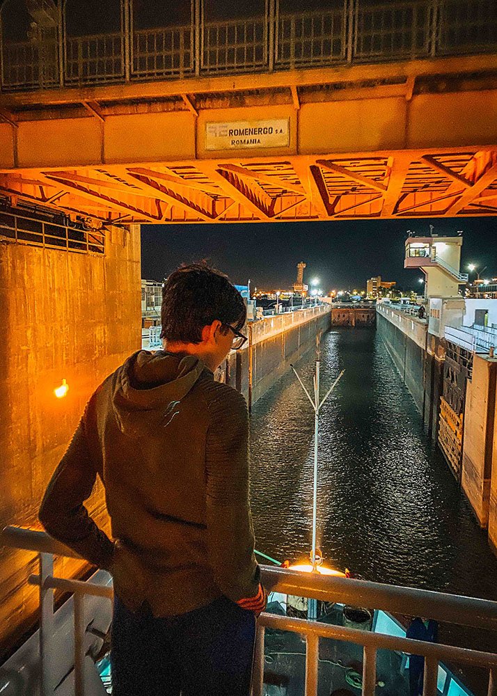 A person looking at a canal lock at night, with the city lights in the background.