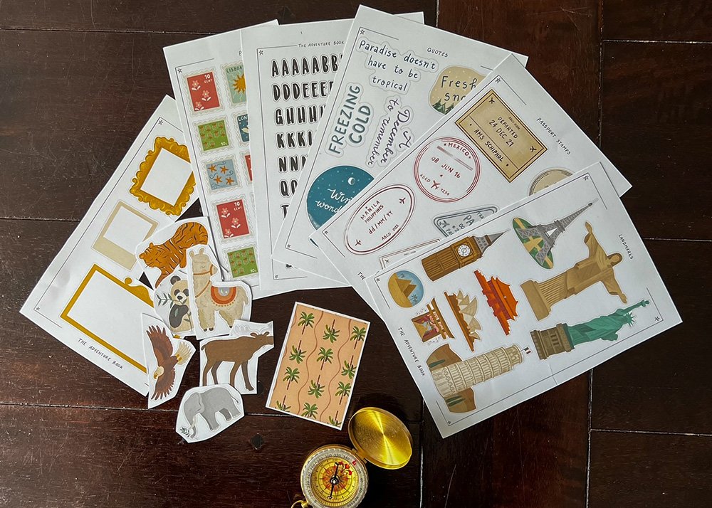A collection of travel-themed stickers, travel stamps and a compass. The items are arranged on a dark surface.