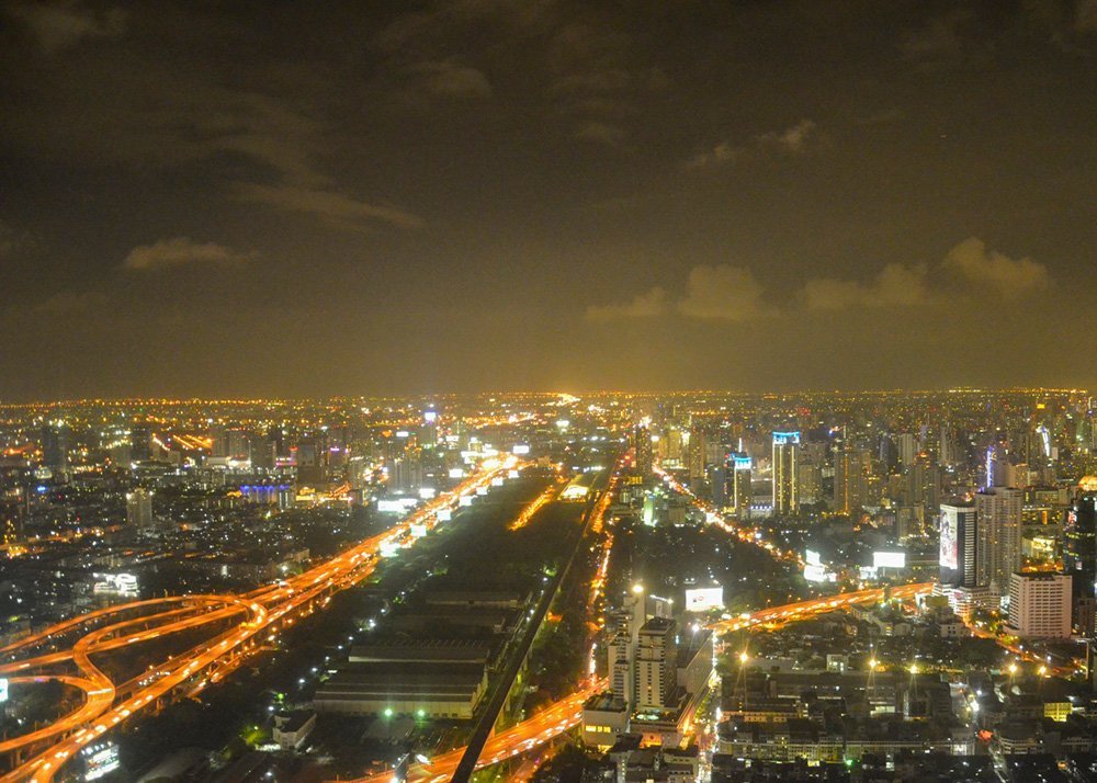 Aerial night view of a city: Aerial view of Bangkok at night, showcasing brightly lit roads and buildings stretching into the distance.