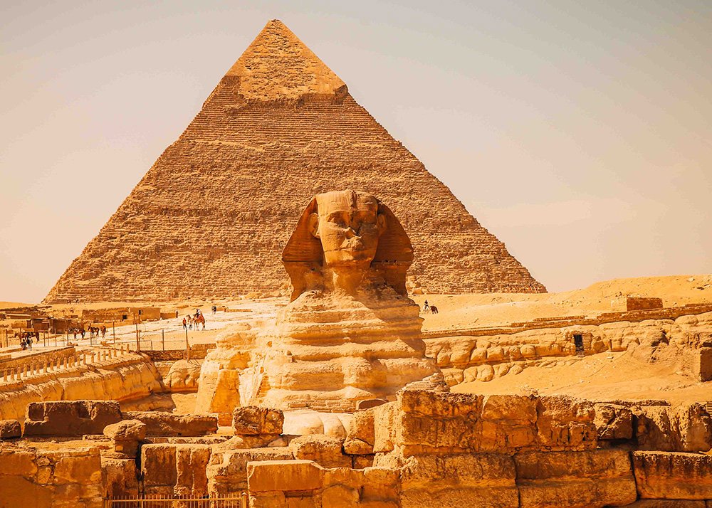 The Great Sphinx of Giza with the Pyramid of Khafre in the background, under a clear sky.