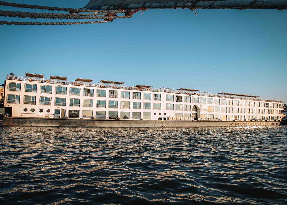 A large white river cruise ship on the Nile River with clear blue skies.