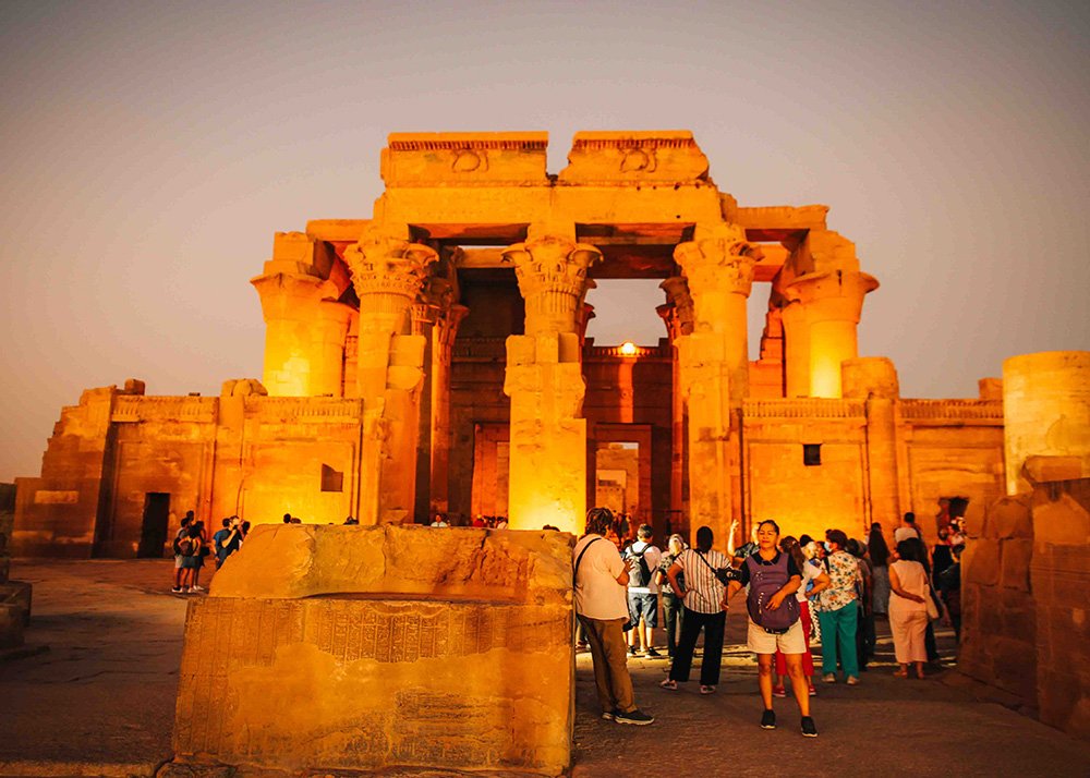 Wide shot of the Kom Ombo Temple entrance with a crowd of tourists in the foreground.