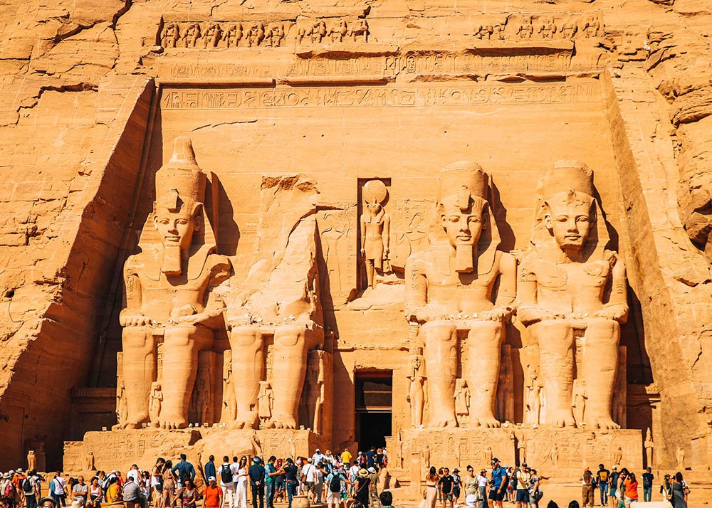View of the Abu Simbel temple with large statues carved into the rock face, surrounded by tourists.