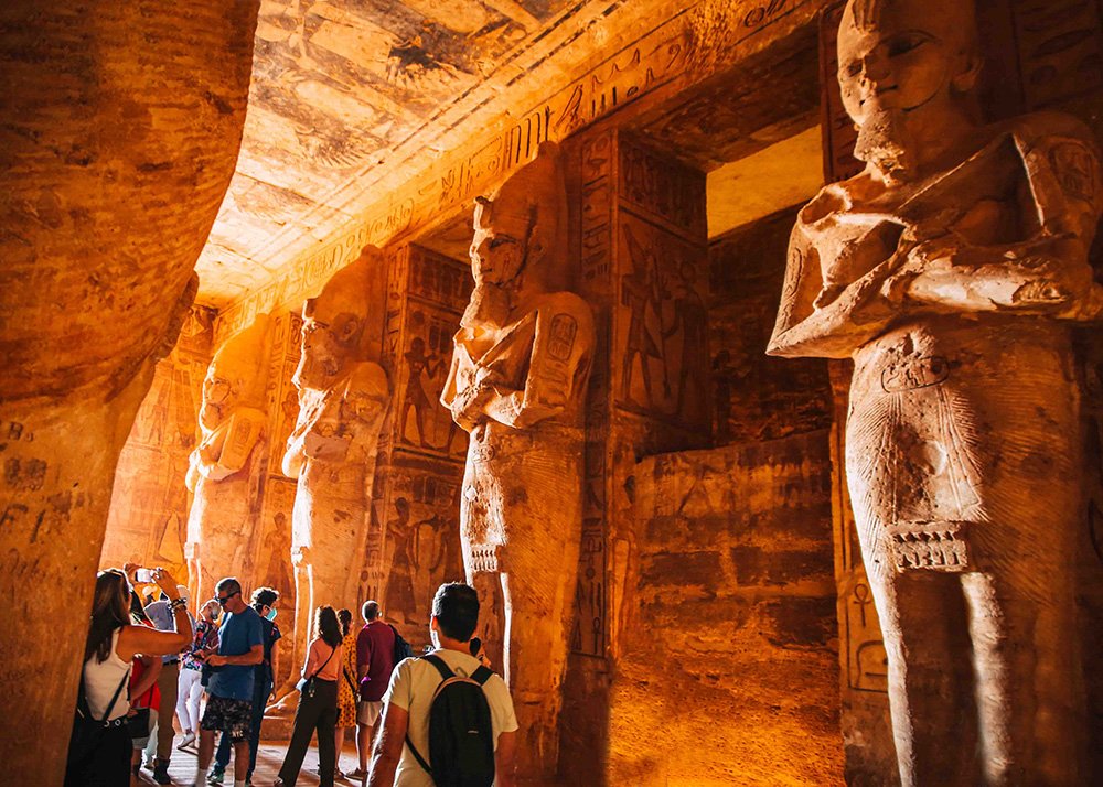A group of tourists exploring the interior of the ancient Egyptian temple Abu Simbel with large statues carved into the walls.