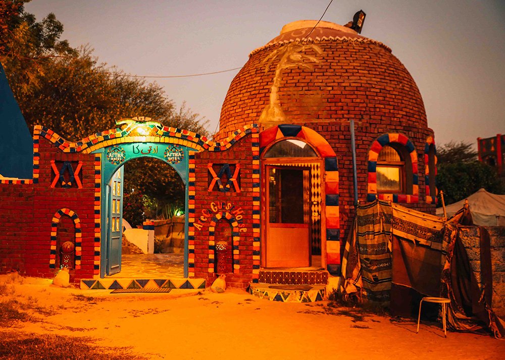 Colorful, dome-shaped guest house with intricate patterns and a welcoming entrance gate, lit up at night.