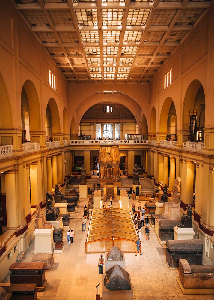 Interior view of the Egyptian Museum in Cairo, showing large statues and artifacts in a spacious hall with a high ceiling.