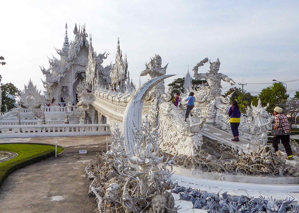The intricate white architecture of Wat Rong Khun, also known as the White Temple, with visitors exploring the structure.