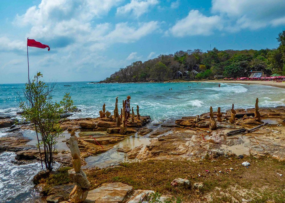 Rocky beach with stone stacks and a red flag in Koh Samet, Thailand.