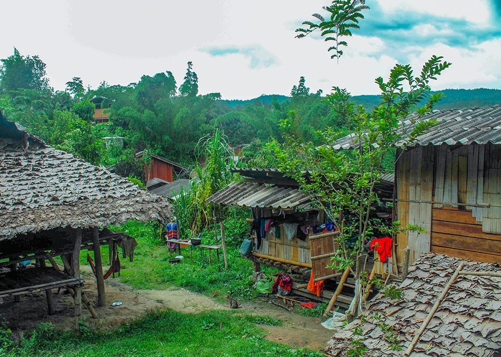 A rural village scene with traditional wooden huts, lush greenery, and people going about their daily activities.