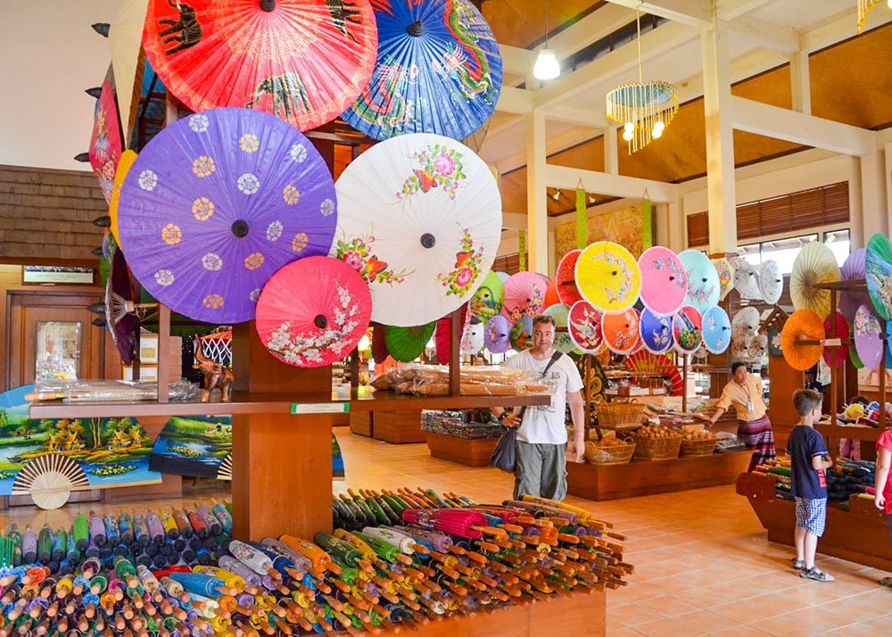 A vibrant shop interior showcasing an array of colorful decorative umbrellas, with a man and children browsing the displays.