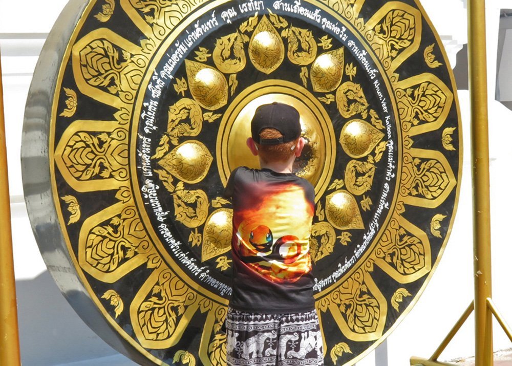 Young boy striking a large decorated gong at Wat Pho in Bangkok.