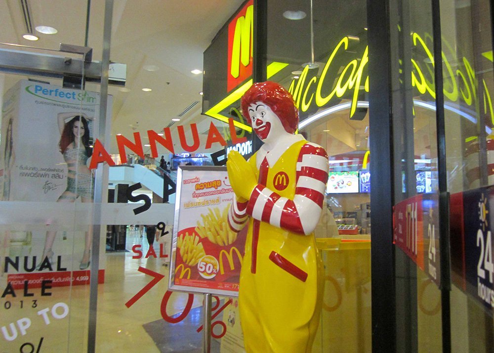 A statue of Ronald McDonald performs a traditional Thai greeting, standing at the entrance of a McDonald's restaurant.