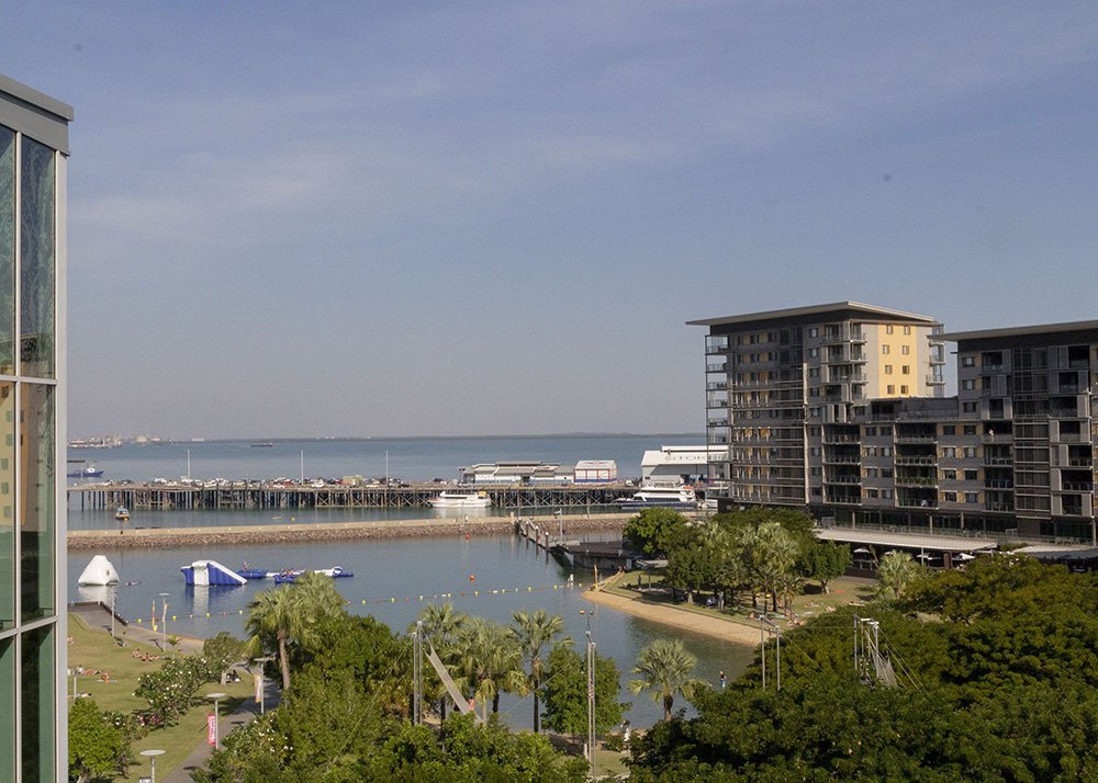 A coastal view of the Darwin marina with boats docked, surrounded by modern buildings and green spaces.