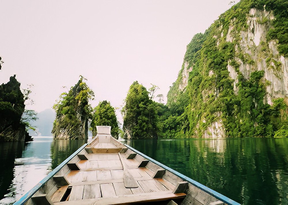 Traditional wooden boat navigating through the emerald waters of Khao Sok National Park, Thailand.
