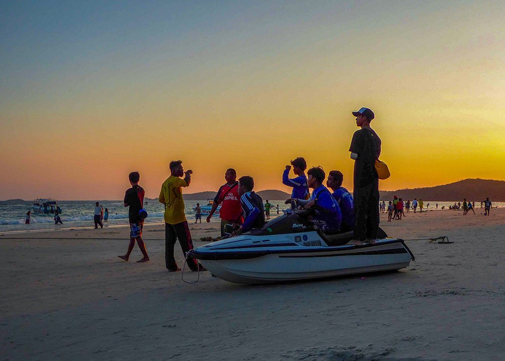 People gathered around a jet ski on the beach at sunset in Koh Samet, Thailand.