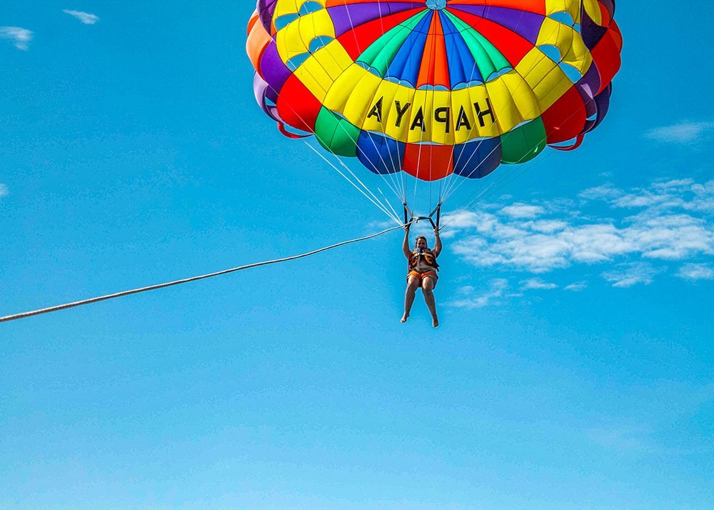 Woman parasailing with a colorful parachute labeled 'HAPPY' against a blue sky.