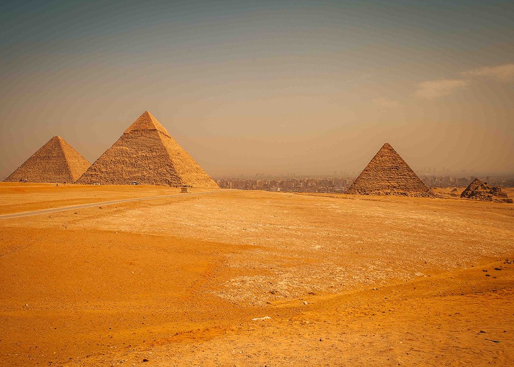 Panoramic view of three pyramids at Giza, including the Great Pyramid, with a vast desert landscape in the foreground.