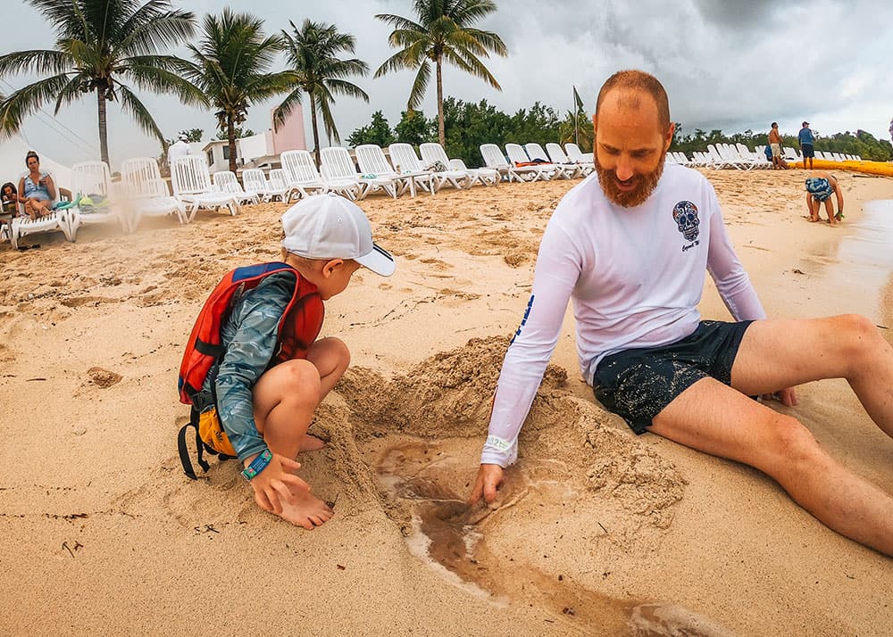 Children are seen playing in the sand at a beach park in Cozumel, Mexico, with the calm sea in the background. The weather is sunny and warm, making it an ideal day for beach activities.