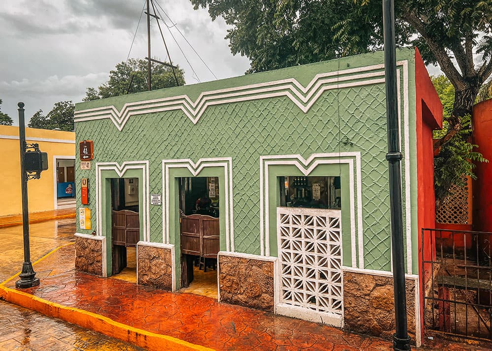 A vibrant green shop in Valladolid, Mexico, with traditional design elements and a wet street from recent rain. The scene captures the charm and color of local architecture.
