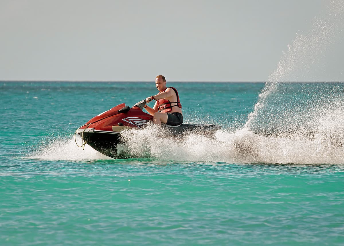 A guy is jetskiing off the coast of Cancun in azure blue waters on a slightly cloudy day