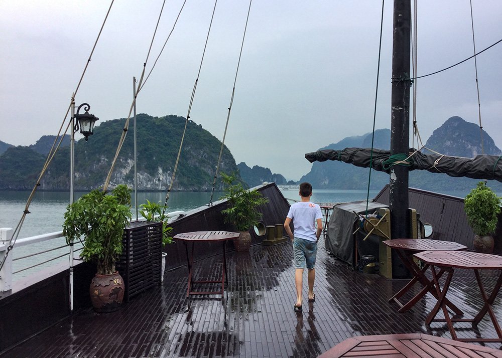 A boy walks on the deck of a Halong Bay cruise ship in Vietnam in the fog: A child walking on the deck of a cruise ship amid the misty backdrop of Halong Bay.