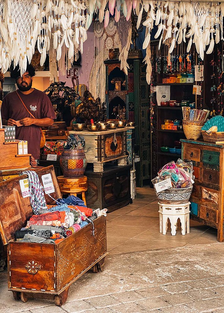 A local shop in Playa del Carmen filled with handcrafted items, textiles, and decorations. The shopkeeper stands among the intricately designed goods, providing a glimpse into the rich culture and artistry of the region.