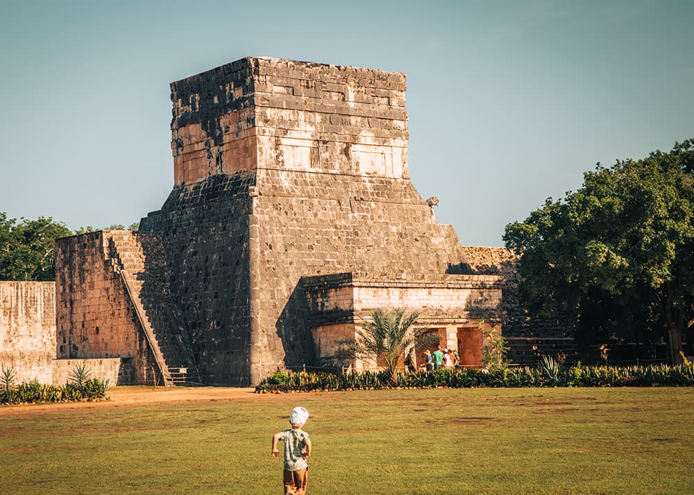 The Temple of the Jaguars at Chichen Itza, Mexico, with its detailed stone carvings and surrounding greenery. A child is seen exploring the area, adding a sense of wonder to the historical site.