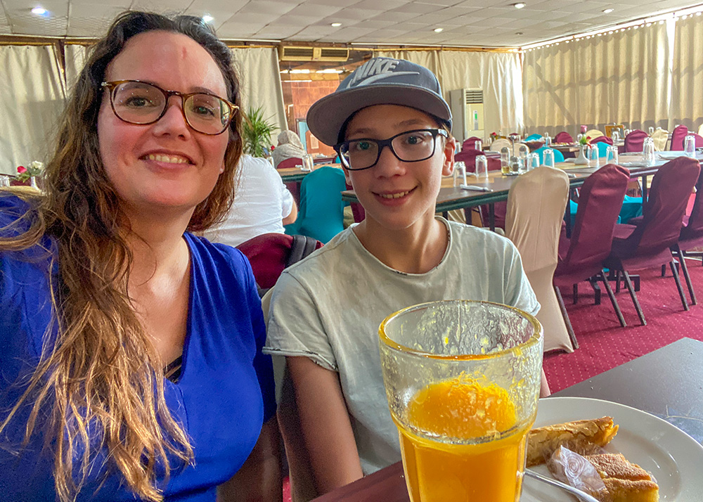 A woman and her son in a restaurant. The boy has Egyptian sweets on his plate and both have fresh pressed juice in front of them.