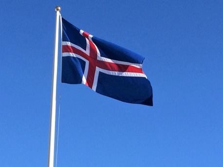The Icelandic flag is raised and moves in the wind giving a clear view on the entire flag. The backdrop is a clear blue sky.