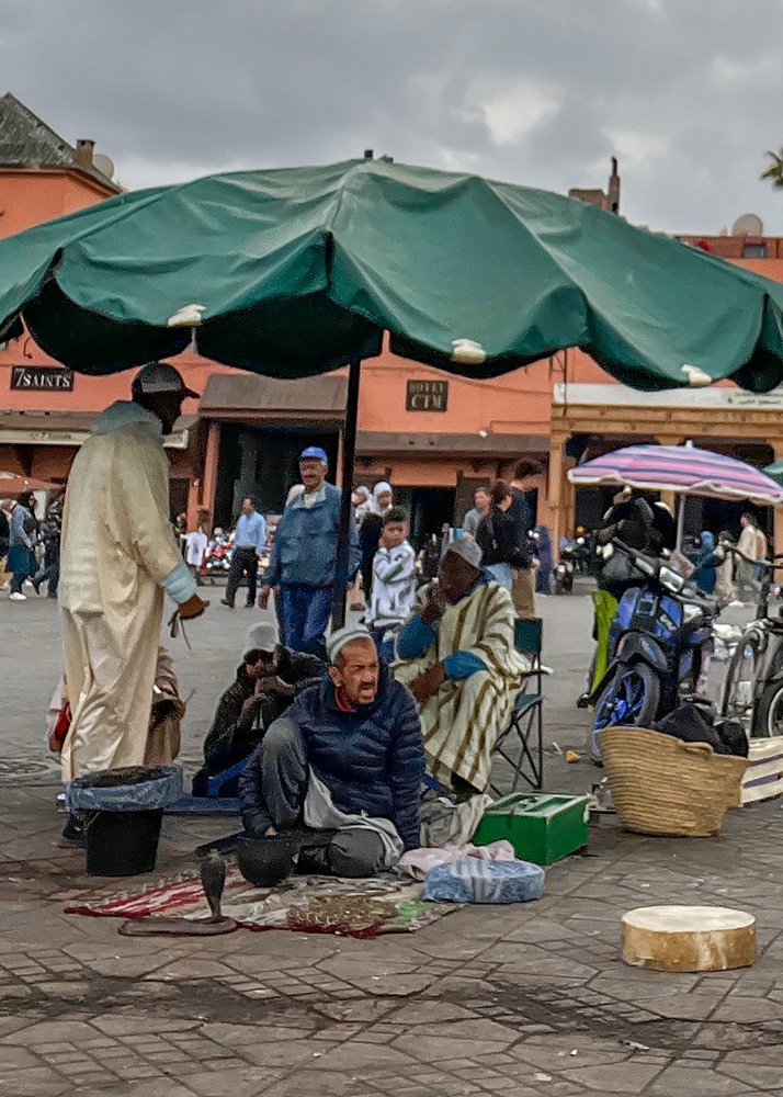 Snake charmers on Jemaa el-Fnaa square in Marrakesh. A cobra and a python can be seen in front of a man sitting on a plate, waiting for customers to perform for.