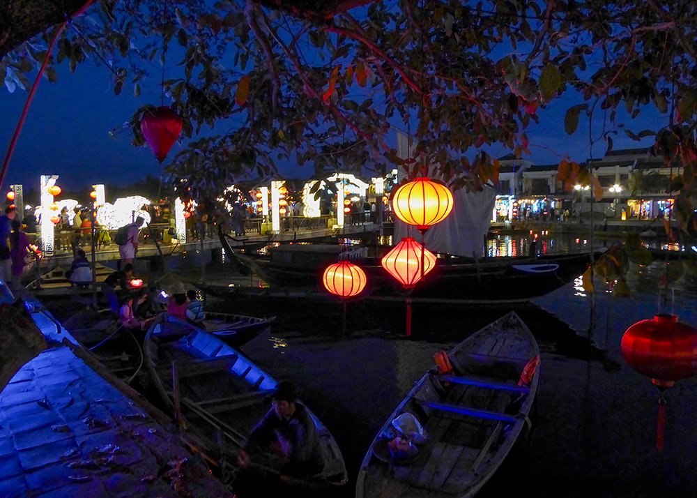 Lanterns are lit along the riverbank in Hoi An and tourists are boarding boats for an evening ride along the river