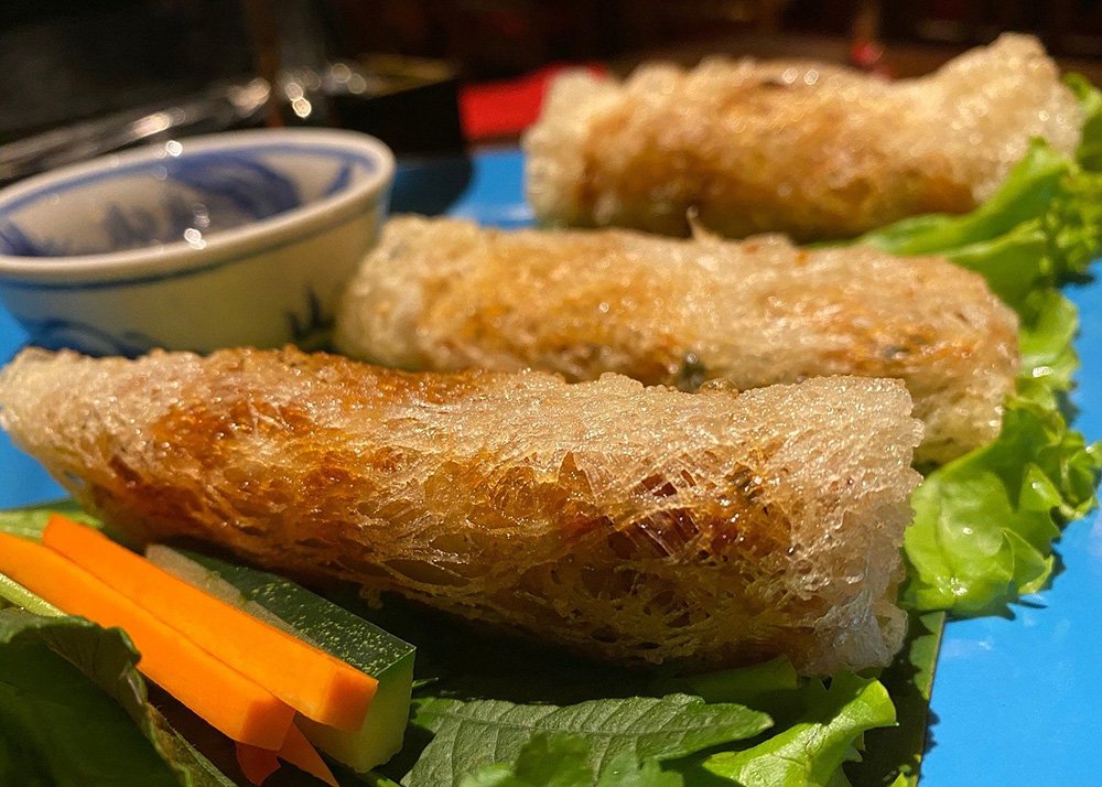 close-up of 3 spring rolls made from rice noodles. Served on a layer of lettuce on a plate.