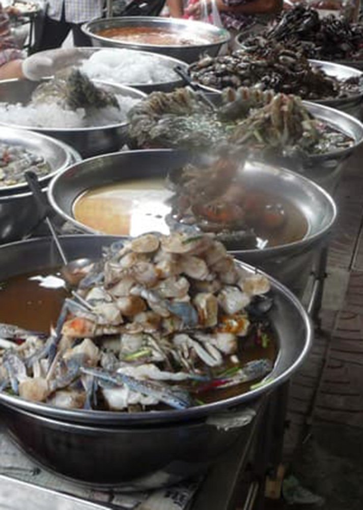 A variety of fresh seafood displayed in metal bowls at Phsar Chas, the Old Market in Siem Reap. The bustling market scene includes crabs, shellfish, and prawns, a vibrant introduction to local ingredients and food culture.