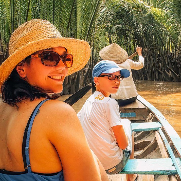 A mother and son in a rowing boat with a woman rowing in the front of the boat in the Mekong Delta.