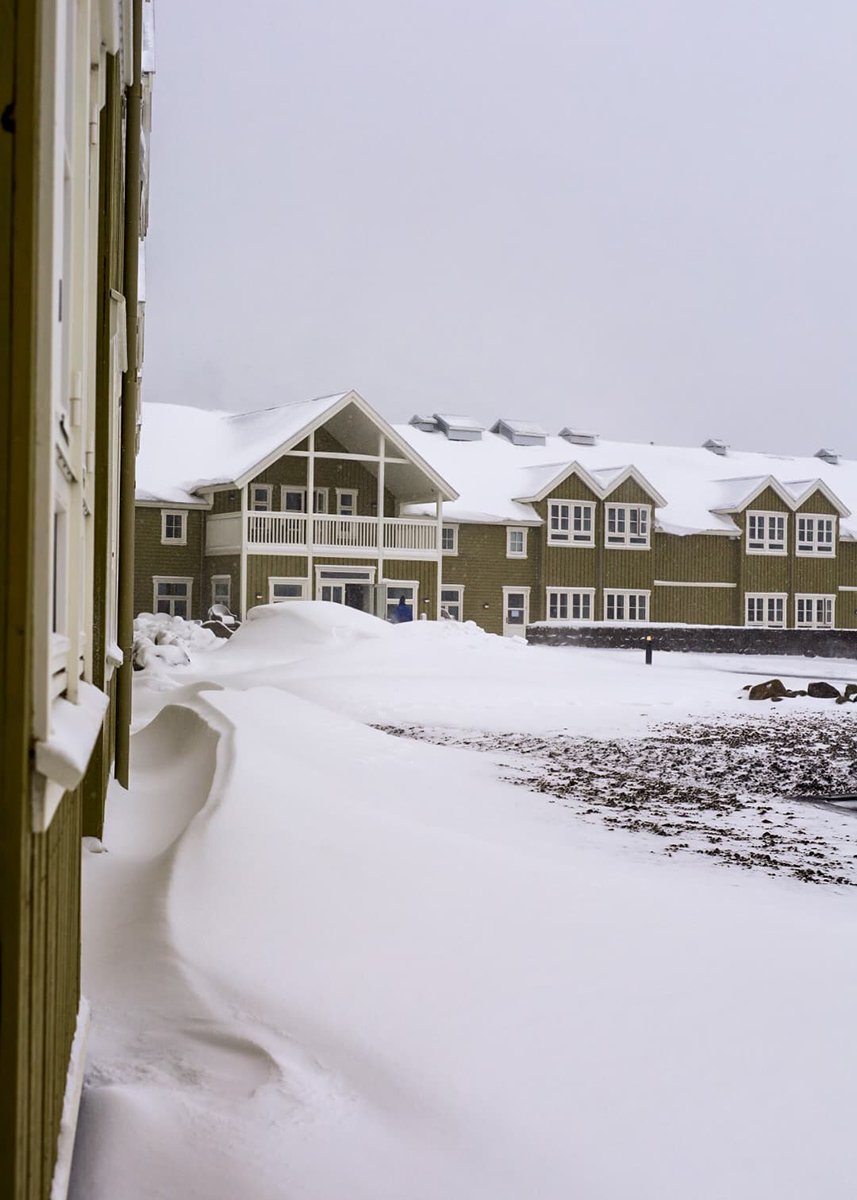 The mosh green Siglo hotel, with white painted window frames is covered and surrounded by snow.