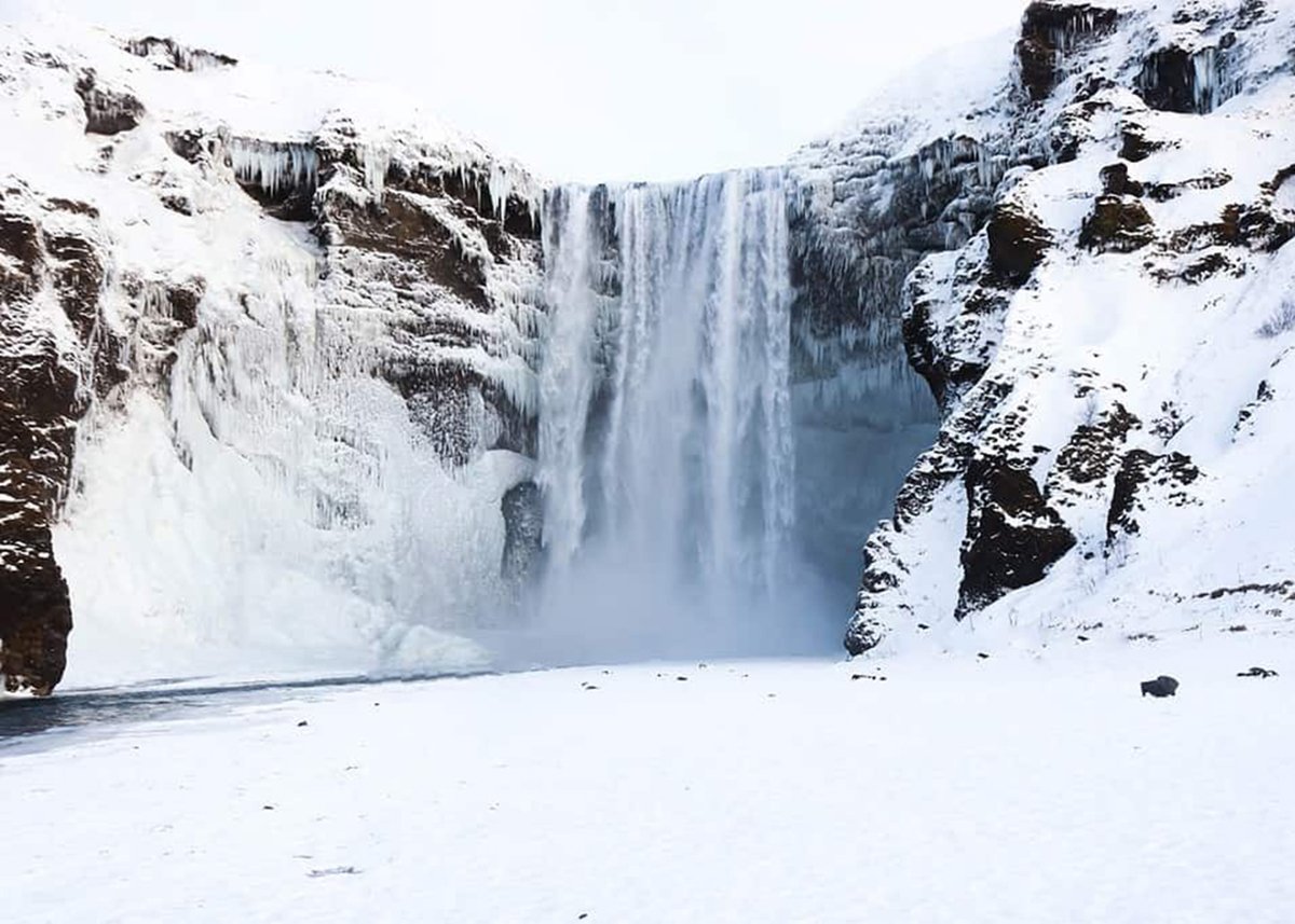 Skogafoss is covered in ice and surrounded by snow