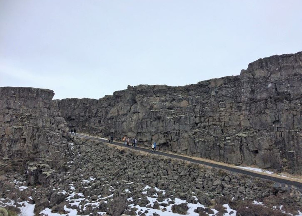 People walk on a small path surrounded by rocks in Thingvellir NP. Bits of snow are visible between the rocks