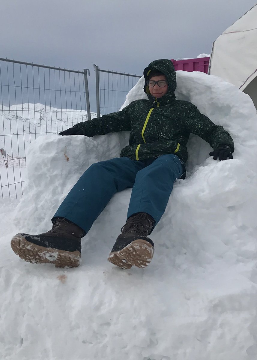 a kid is all dressed up in winter gear and chilling in a chair made of snow