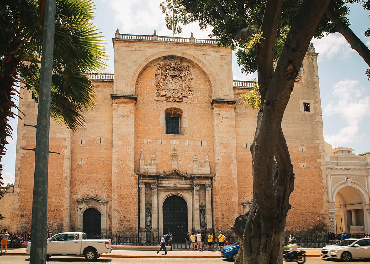 Front view of Mérida Cathedral with colonial stone facade, tall arched doorway, and sunny sky.