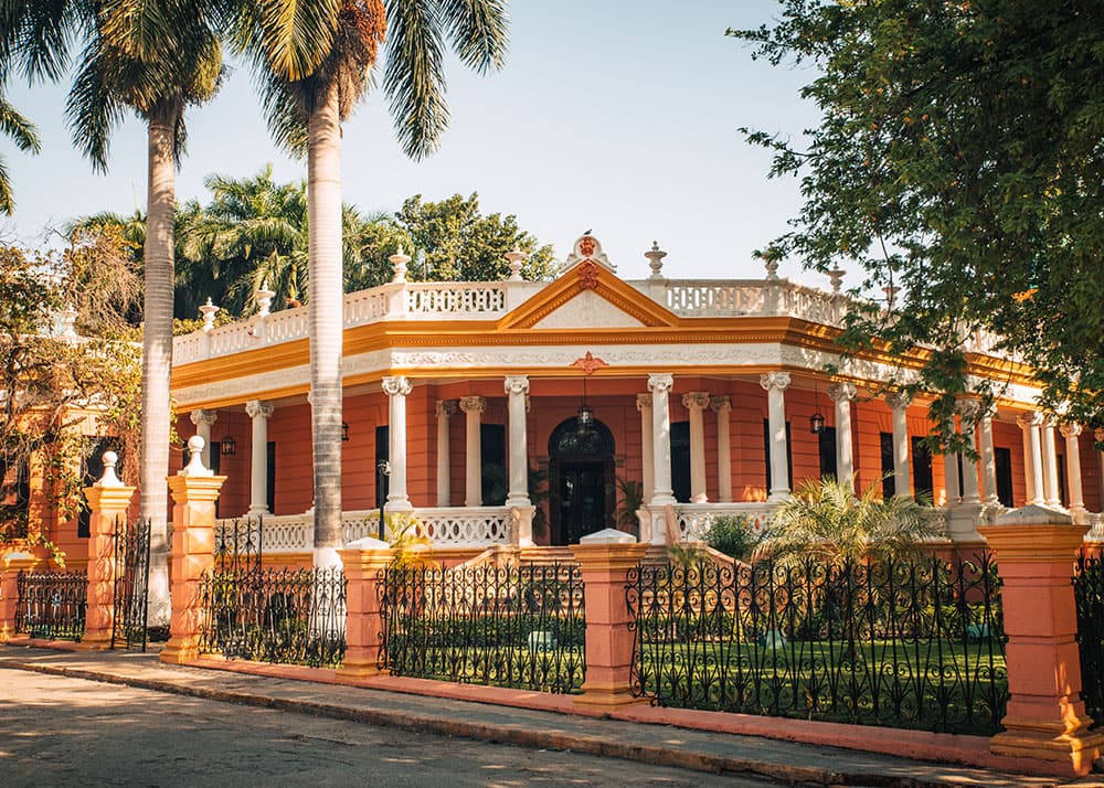 Bright orange colonial-era mansion with palm trees along Paseo de Montejo in Mérida.