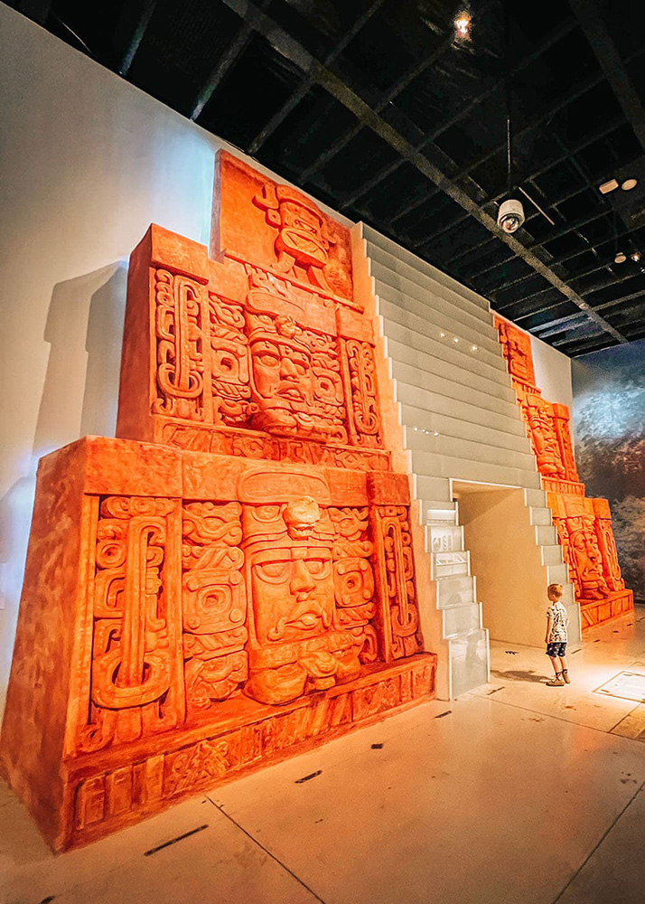 Child explores a bright orange Mayan pyramid replica inside Gran Museo del Mundo Maya in Mérida.