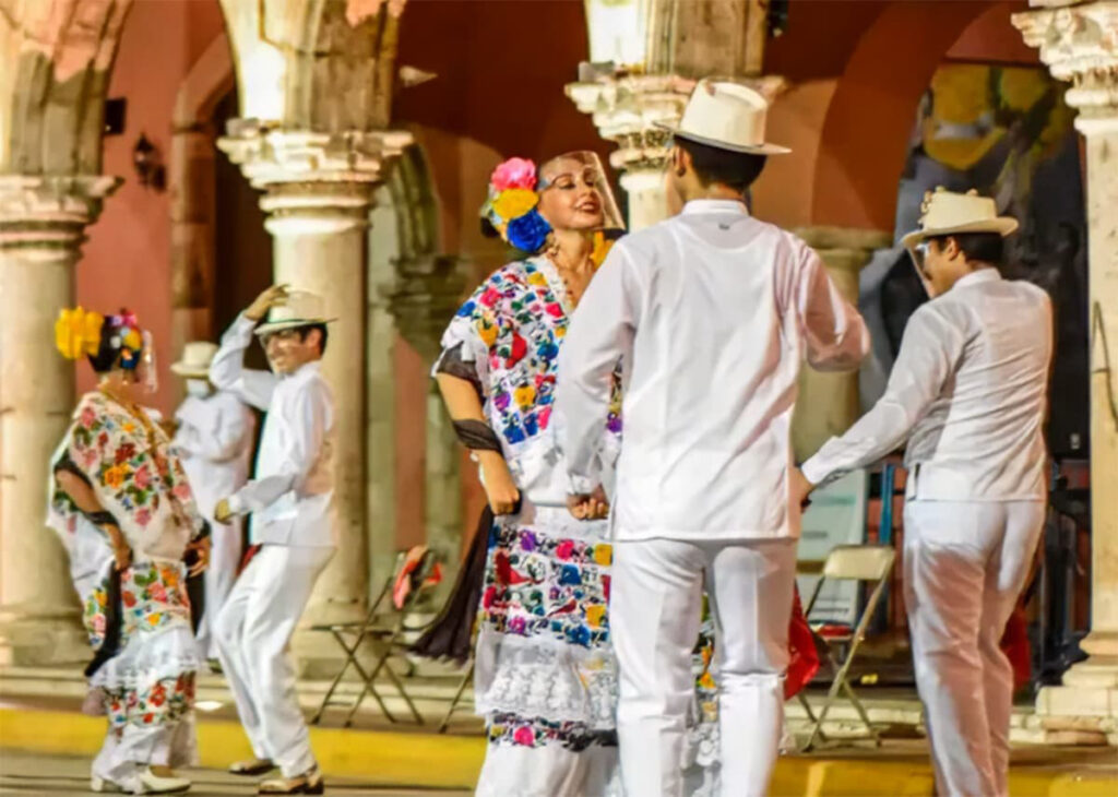 Dancers in white clothing and floral huipils perform folkloric Yucatecan dance under stone arches in Mérida.