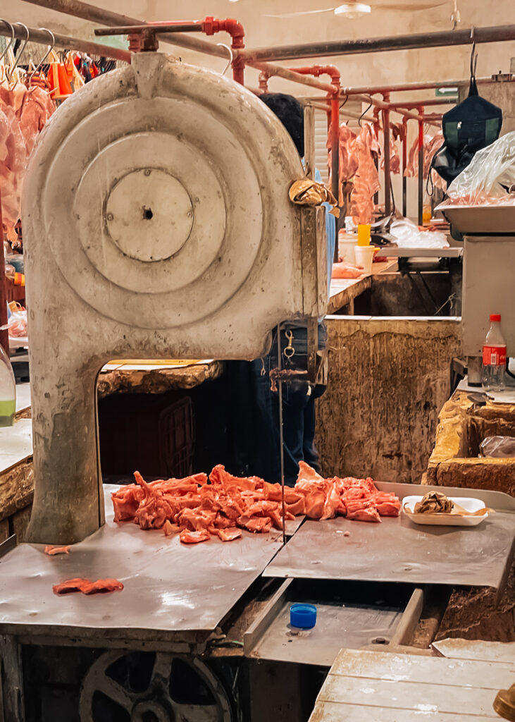 Raw meat and a bandsaw on a butcher’s table inside Mérida’s bustling traditional market.