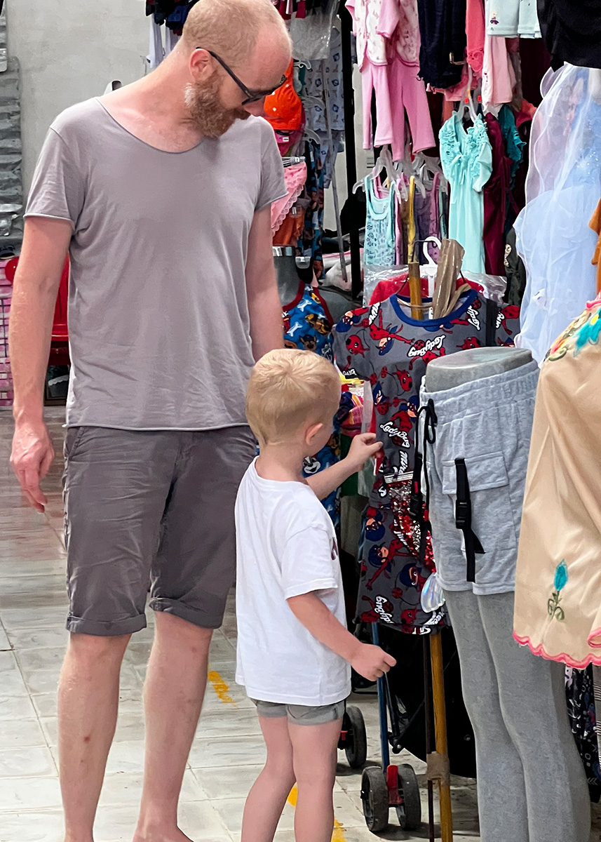Father and child browse colorful kids’ clothes inside a local clothing stall in a Mérida indoor market.