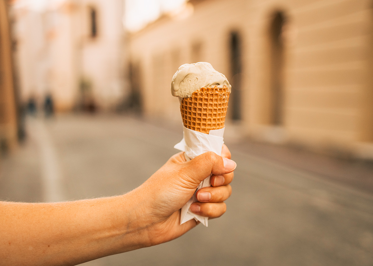 Hand holding a melting ice cream cone on a blurred street in Mérida’s historic center during golden hour.