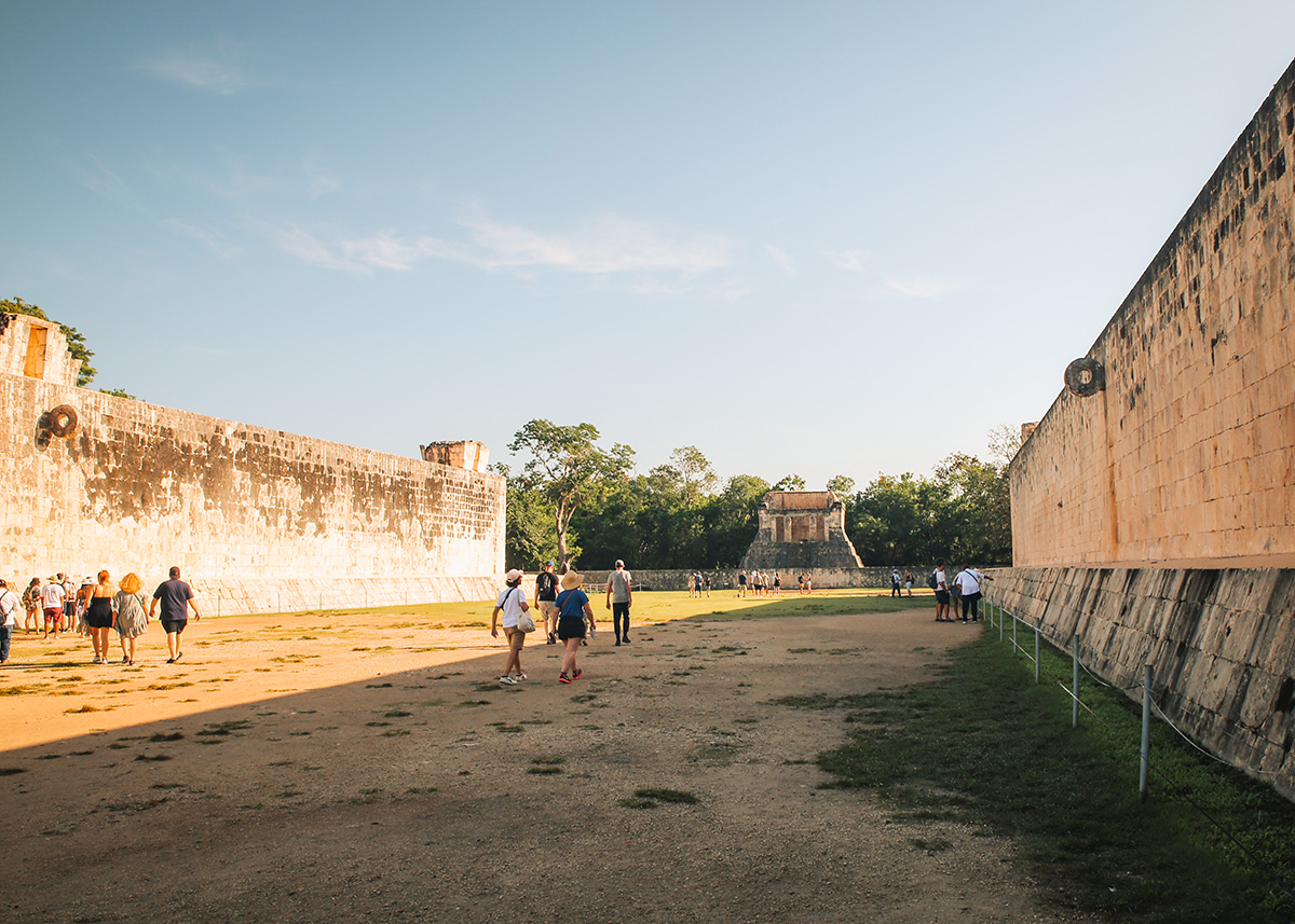 View of the ancient Pok Ta Pok ball court at Chichén Itzá with stone rings on high walls and tourists walking the field.